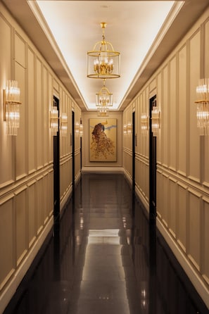 A long, elegant hallway with a chandelier, wall sconces, and a large painting.