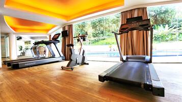 A gym with treadmills and an elliptical machine, large windows with curtains, and a view of greenery outside.