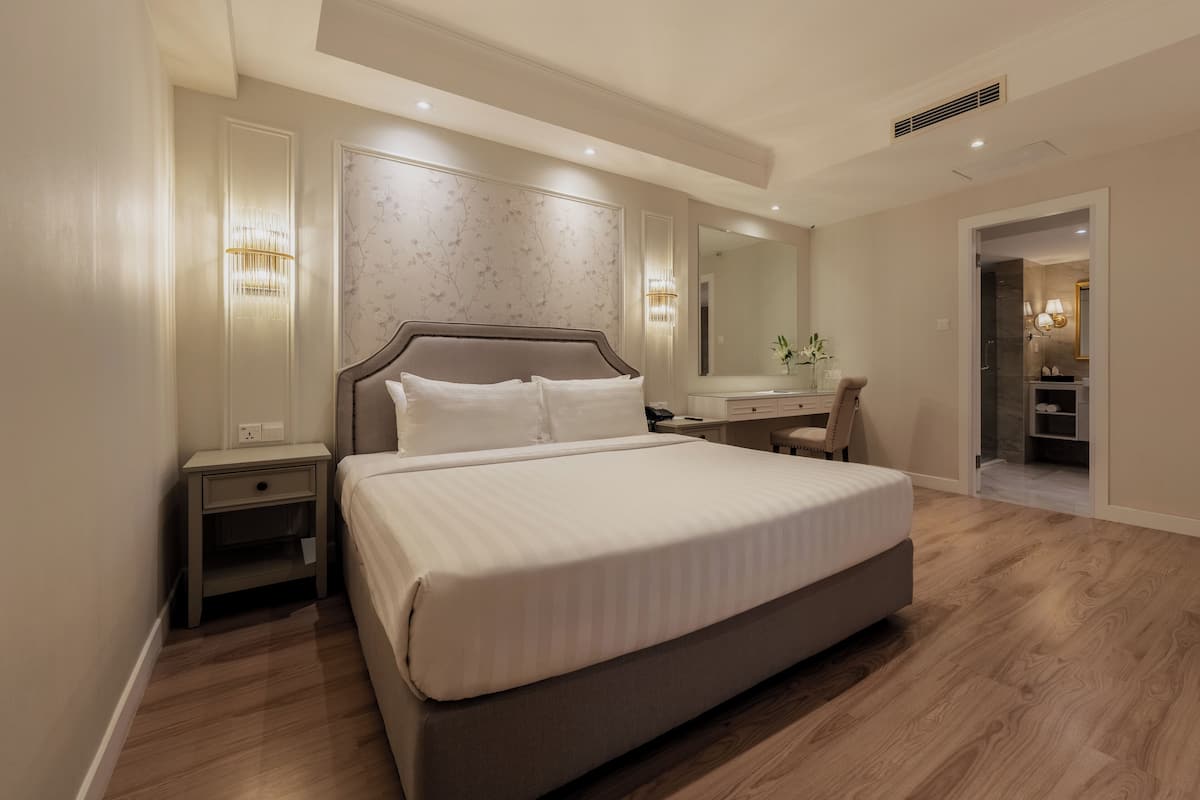 Ein modernes Hotelzimmer mit einem großen Bett, Nachttischen, einem Schminktisch mit Spiegel und einem begehbaren Kleiderschrank.