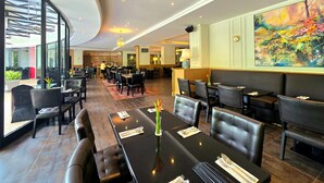 Un restaurant spacieux avec de hauts plafonds, un éclairage moderne et un grand tableau accroché au mur.