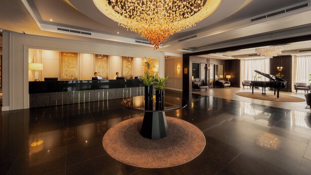 Un hall d’entrée spacieux, doté d’un comptoir d’accueil, d’un grand piano et d’un imposant lustre.