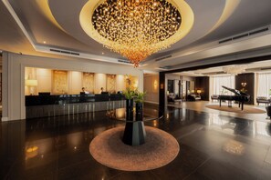 A spacious lobby with a reception desk, a grand piano, and a large chandelier.