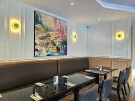 Un restaurante con una larga zona de asientos tipo banco, mesas con sillas y un cuadro abstracto grande en la pared.
