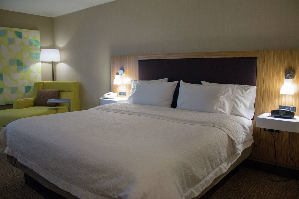 Une chambre d’hôtel avec un grand lit, une table de chevet avec une lampe, une chaise et un téléphone fixé au mur.
