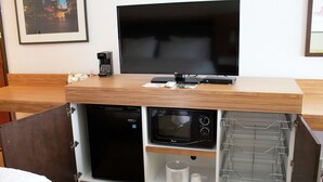 A compact kitchenette with a microwave, coffee maker, and a flat-screen TV on a wooden countertop.