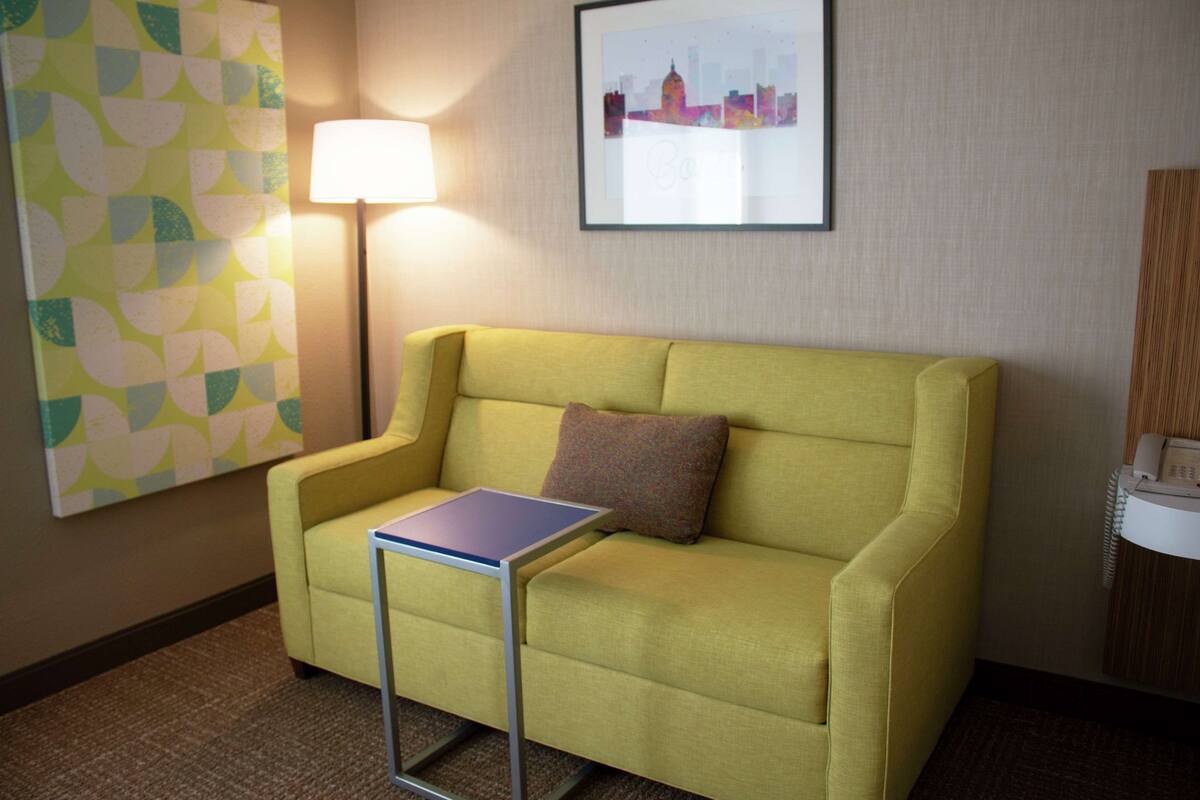 Un canapé jaune, accompagné d ’une petite table, d’un coussin, d’une lampe et d’un tableau encadré accroché au mur.