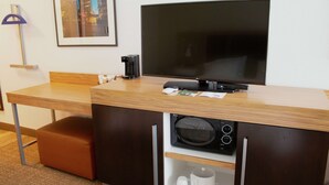 A modern hotel room with a wooden desk, a flat-screen TV, a microwave, and a coffee maker.