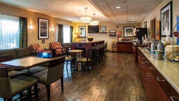 A hotel dining area with a long counter, multiple seating options including booths and tables, a bar area, and a kitchen visible in the background.