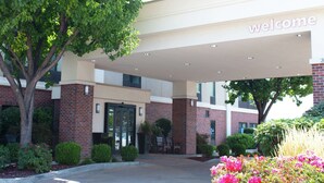 A building entrance with a 'welcome' sign, brick walls, and a tree.