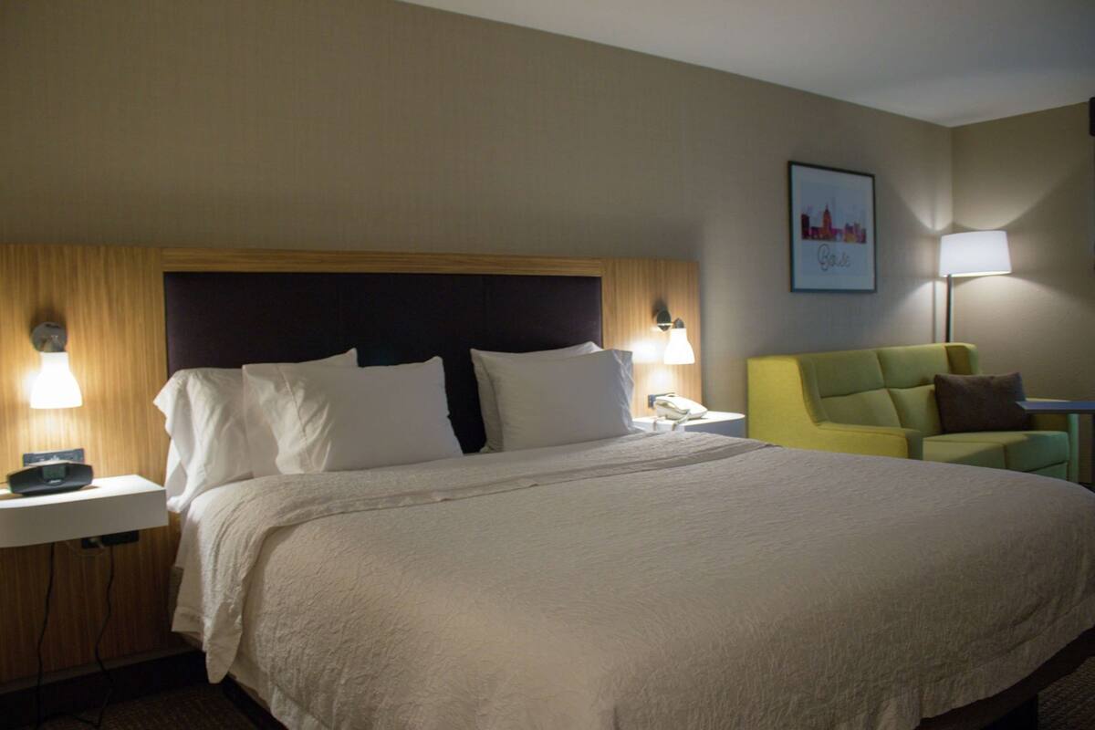 A hotel room with a large bed, bedside tables, a chair, and a wall-mounted lamp.