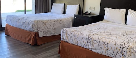 A hotel room with two beds, each with a patterned bedspread and brown bed skirt. There is a nightstand with a phone and a framed picture on the wall.