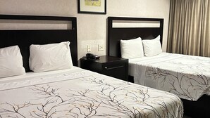 Quarto de hotel com duas camas, cada uma com roupa de cama branca e padrão de galhos de árvore. Há um quadro na parede e uma mesa de cabeceira com um telefone e um abajur.