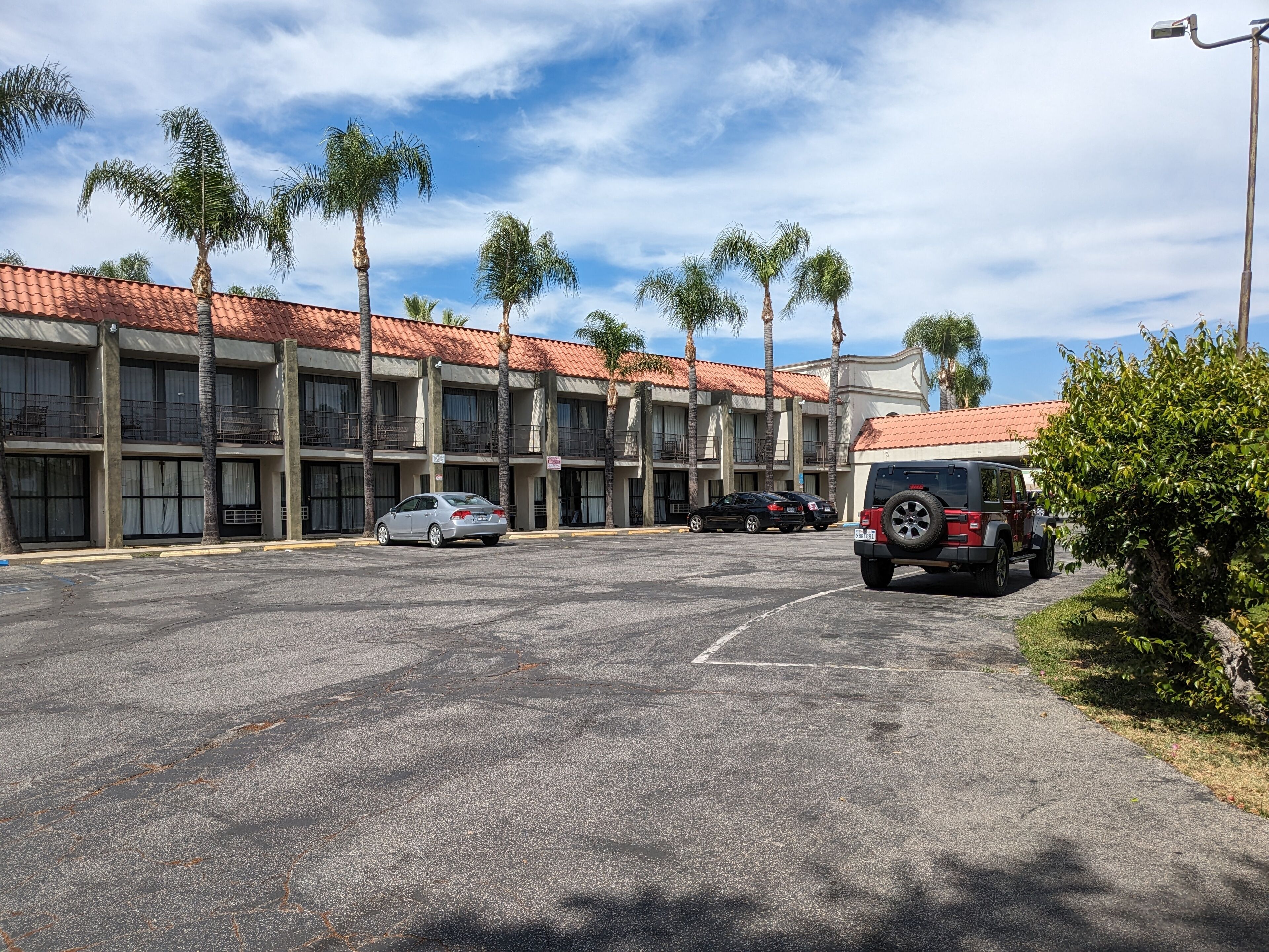 A parking lot with a building featuring a red-tiled roof and multiple balconies.