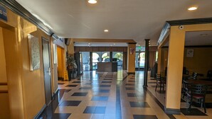 Um hall de hotel com padrão de piso quadriculado, uma mesa de recepção e uma área de estar com mesas e cadeiras.