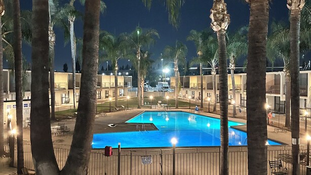 Vista noturna de uma piscina rodeada por palmeiras e um caminho.
