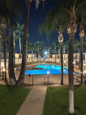 A nighttime view of a swimming pool surrounded by palm trees and a walkway. - Valley Inn (Mission Hills)