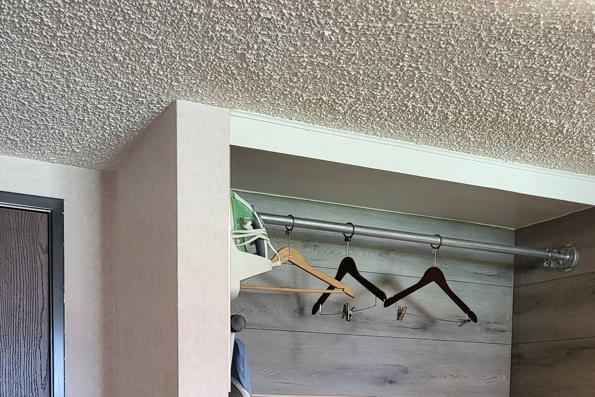 A room with a wooden floor, a black storage unit with drawers, a coat rack with hangers, and a door with a privacy sign.