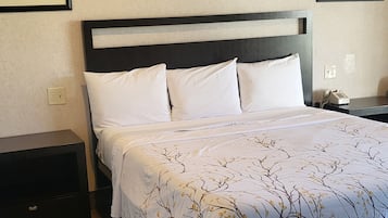 Un letto rifatto con cura, con copriletto decorato, una testiera scura e cuscini bianchi. Sono presenti due comodini, uno per lato del letto. La stanza ha un pavimento in legno e un soffitto strutturato.