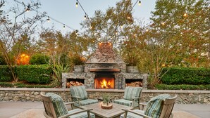 An outdoor patio with a stone fireplace, green-striped chairs, and string lights.