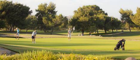 A golf course with players, a stroller, and a stream.