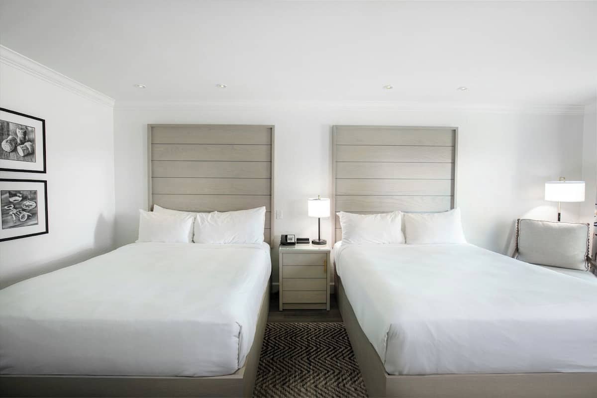 A hotel room with two single beds, a nightstand with a lamp, and framed pictures on the wall.