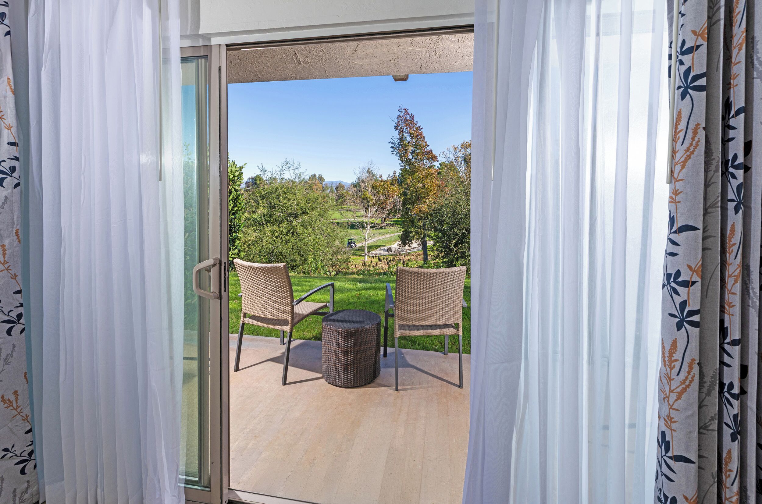 A glass door leading to an outdoor patio with wicker furniture and a round table.