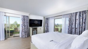 A hotel room with a large bed, a flat-screen TV mounted on the wall, and a balcony with curtains.