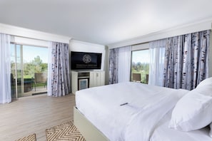 A hotel room with a large bed, a flat-screen TV mounted on the wall, and a balcony with curtains.