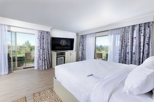 Una habitación de hotel con una cama grande, un televisor de pantalla plana en la pared y un balcón con cortinas.