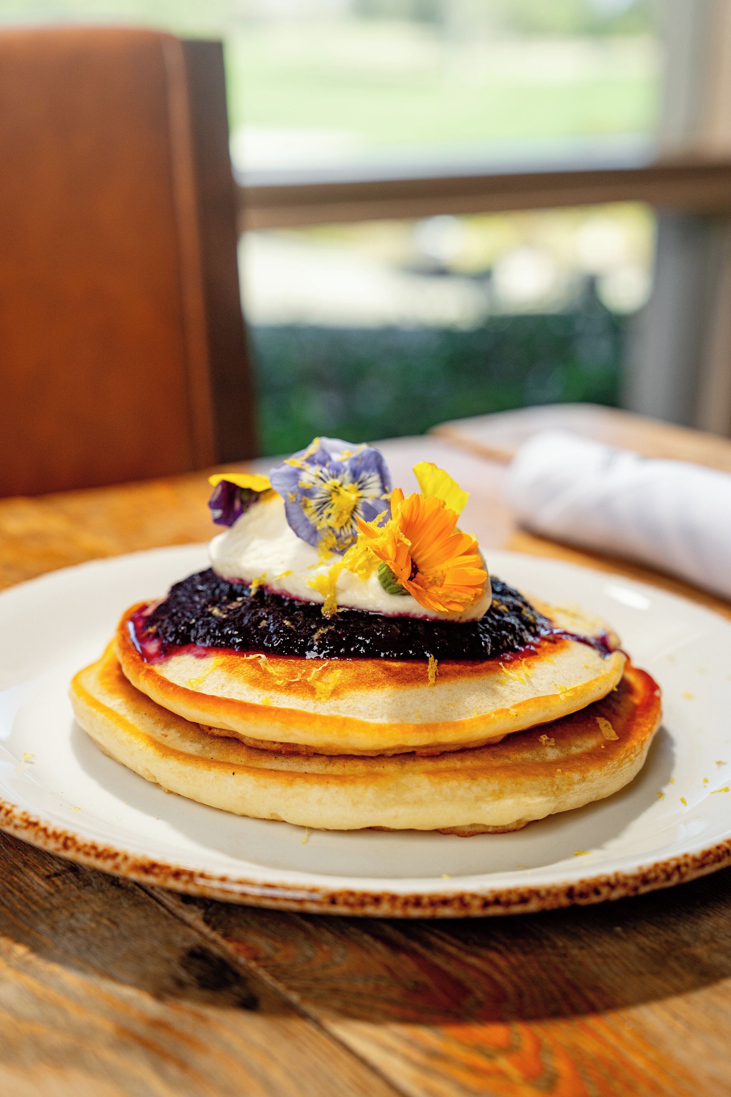 A stack of pancakes with a berry compote and a decorative flower on a white plate.