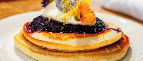 A stack of pancakes with a berry compote and a decorative flower on a white plate.