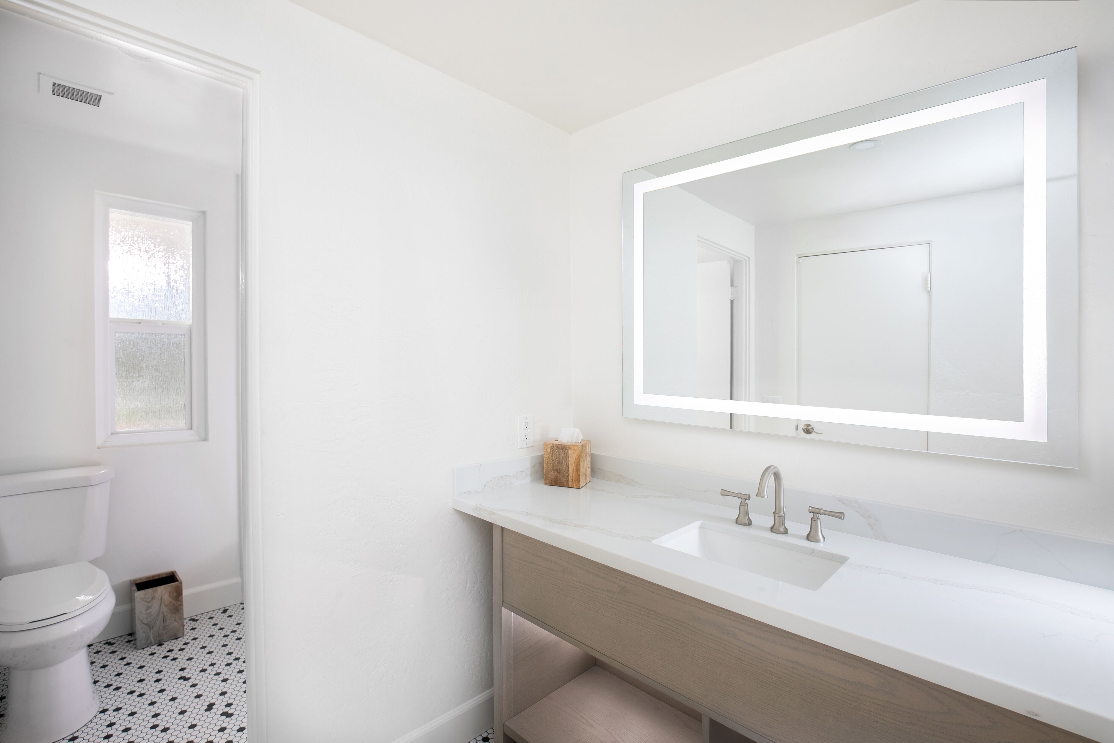A modern bathroom with a white sink, a mirror, and a toilet.