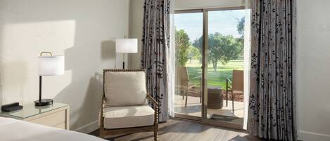 A hotel room with a bed, a chair, a lamp, and a view of a golf course through a sliding glass door.