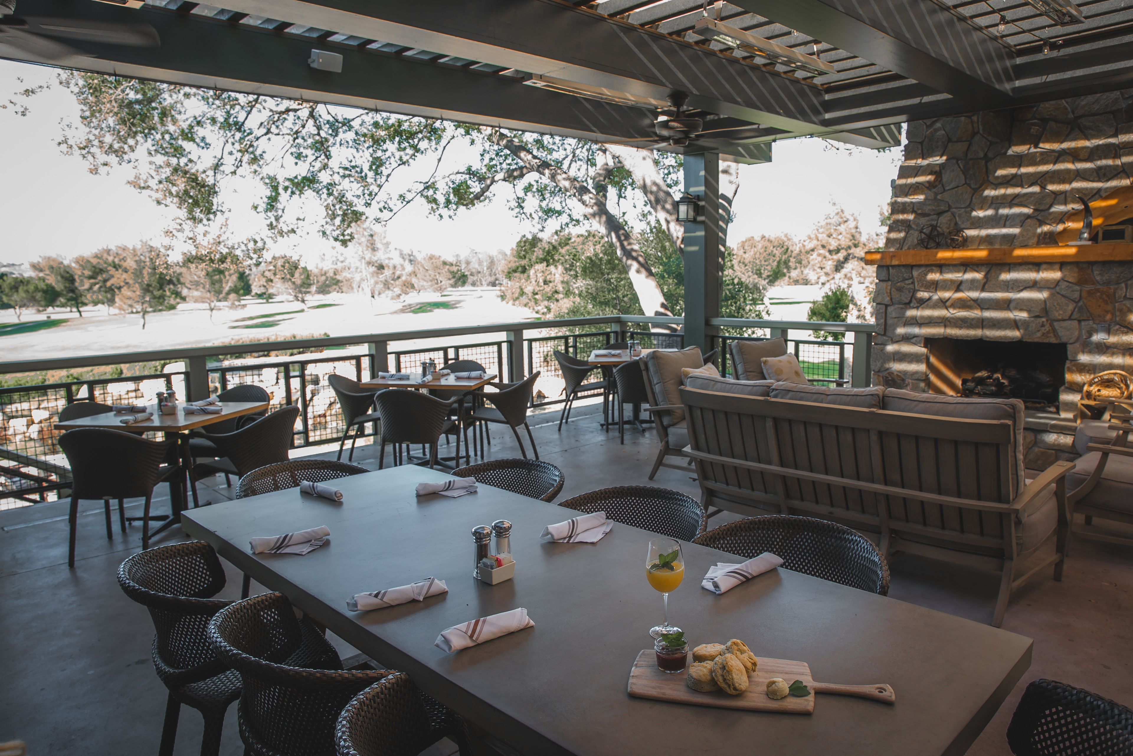 An outdoor patio area with tables and chairs, a stone fireplace, and a view of a body of water.