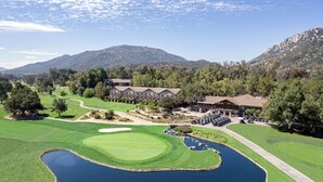 Un parcours de golf doté d’un club-house, d’un étang et avec des montagnes en toile de fond.