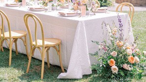 Un espace de restauration en plein air avec une longue table dressée pour un repas, entourée de chaises et décorée de fleurs et de bougies.