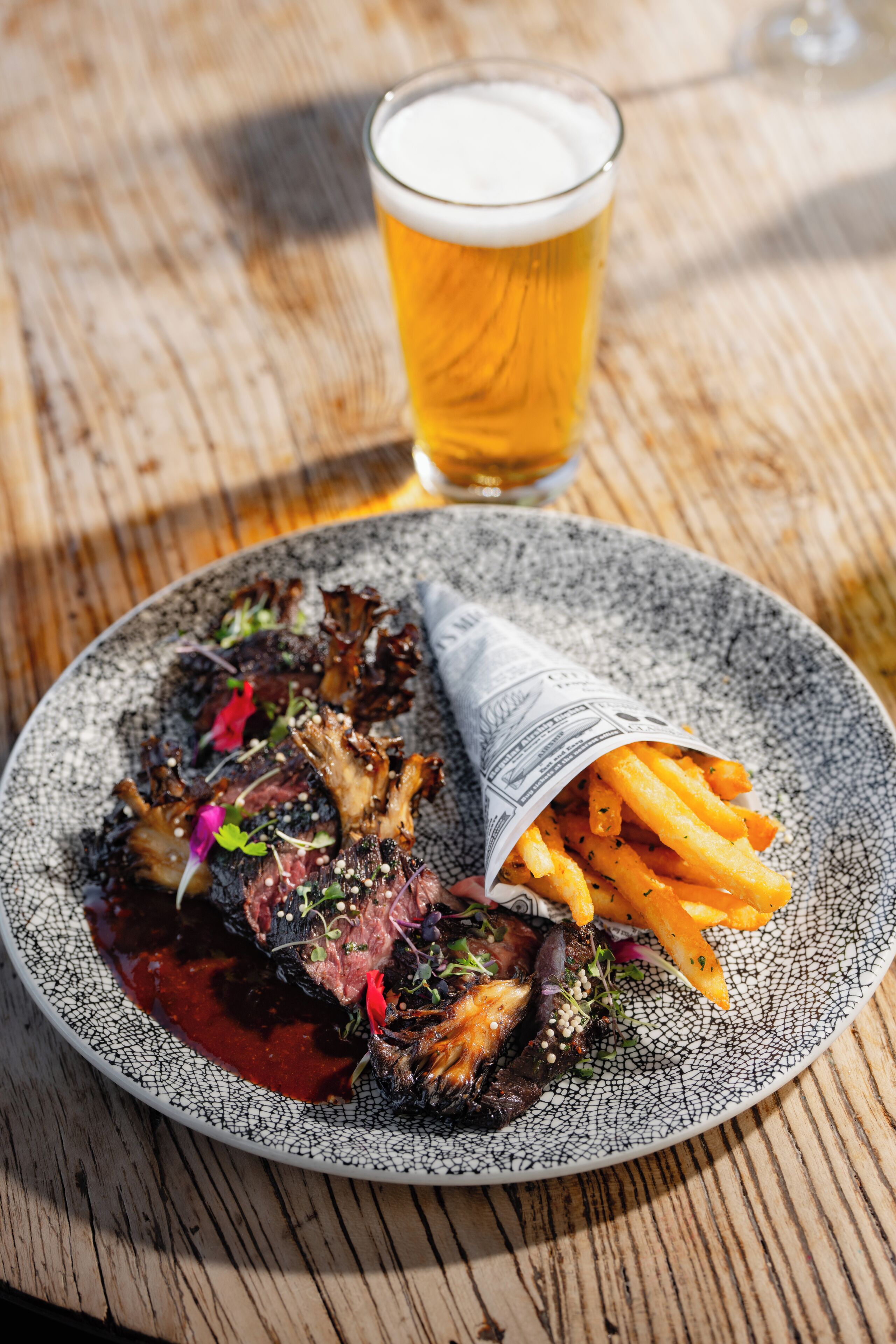 Un plato de comida con un vaso de cerveza sobre una mesa de madera.