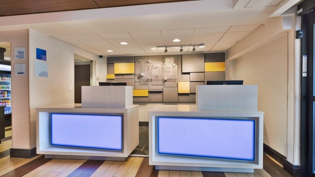 Zona de recepción de hotel con diseño moderno, que incluye un mostrador de check-in, un área de espera con asientos y una tienda a la vista al fondo.
