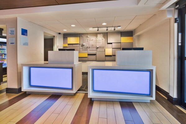 Un'area reception di un hotel dal design moderno, con una scrivania per il check-in, una zona d'attesa con posti a sedere e un negozio ben visibile sullo sfondo.