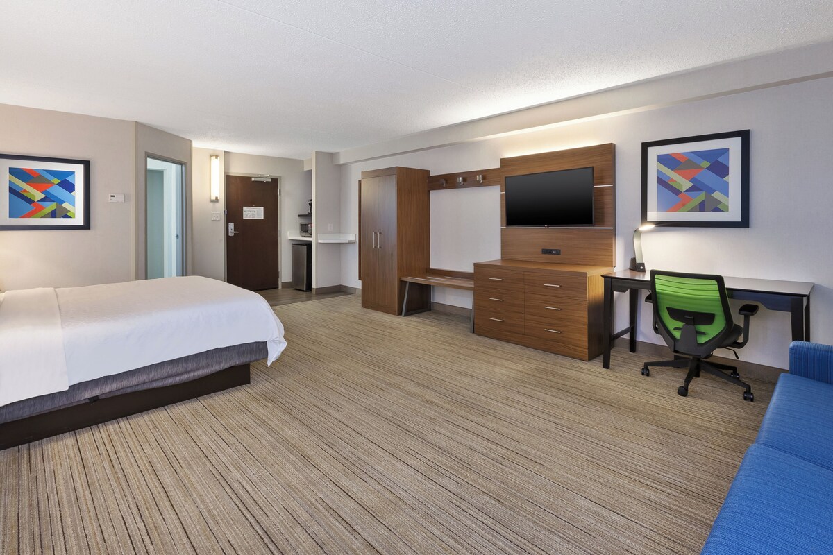 Camera d'hotel con due letti, una scrivania con un computer, una TV e una sedia da ufficio verde.