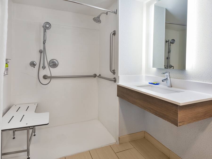 A bathroom with a shower, a sink with a mirror, and a grab bar.
