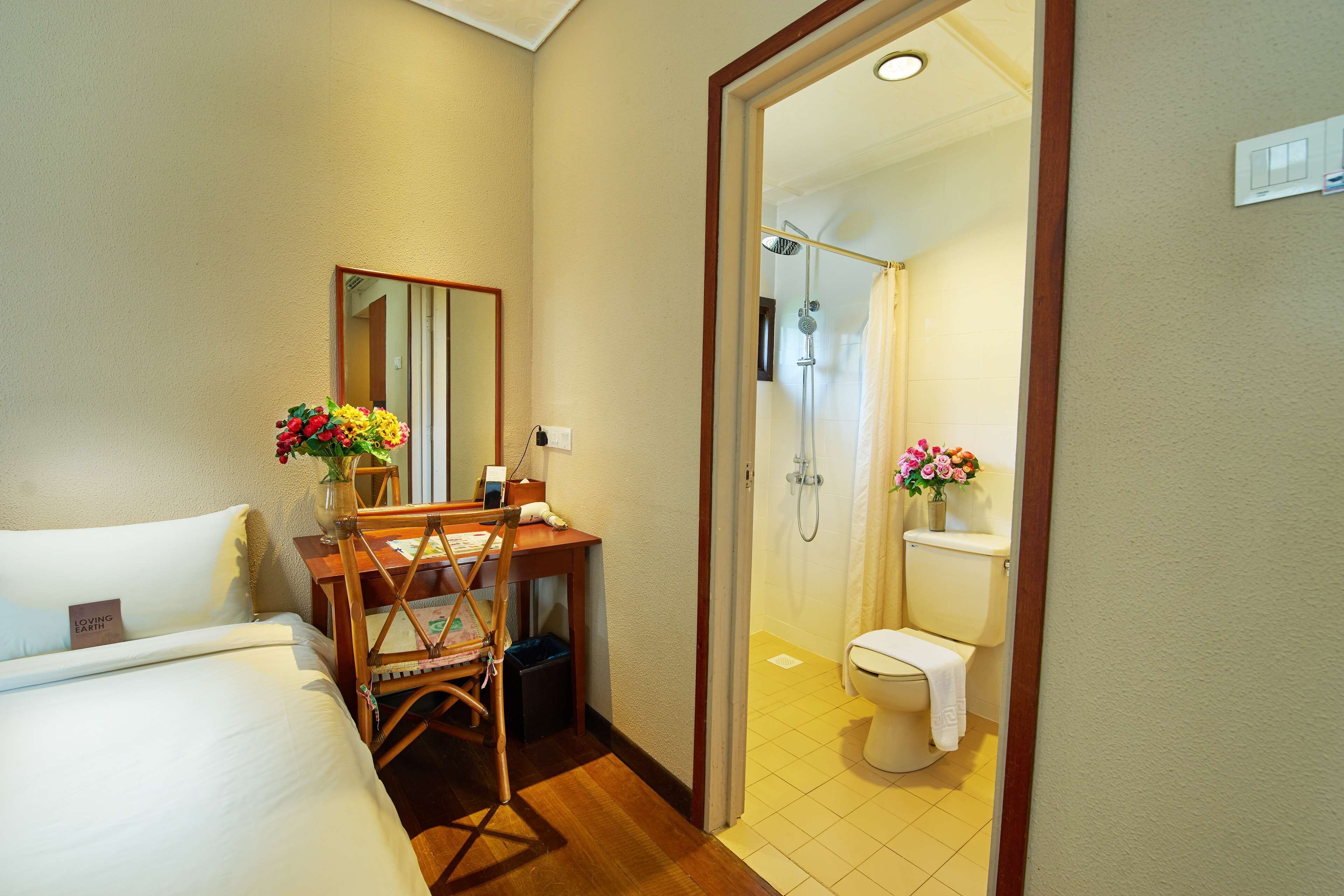 Habitación de hotel con cama, escritorio con silla, espejo, ducha y retrete.