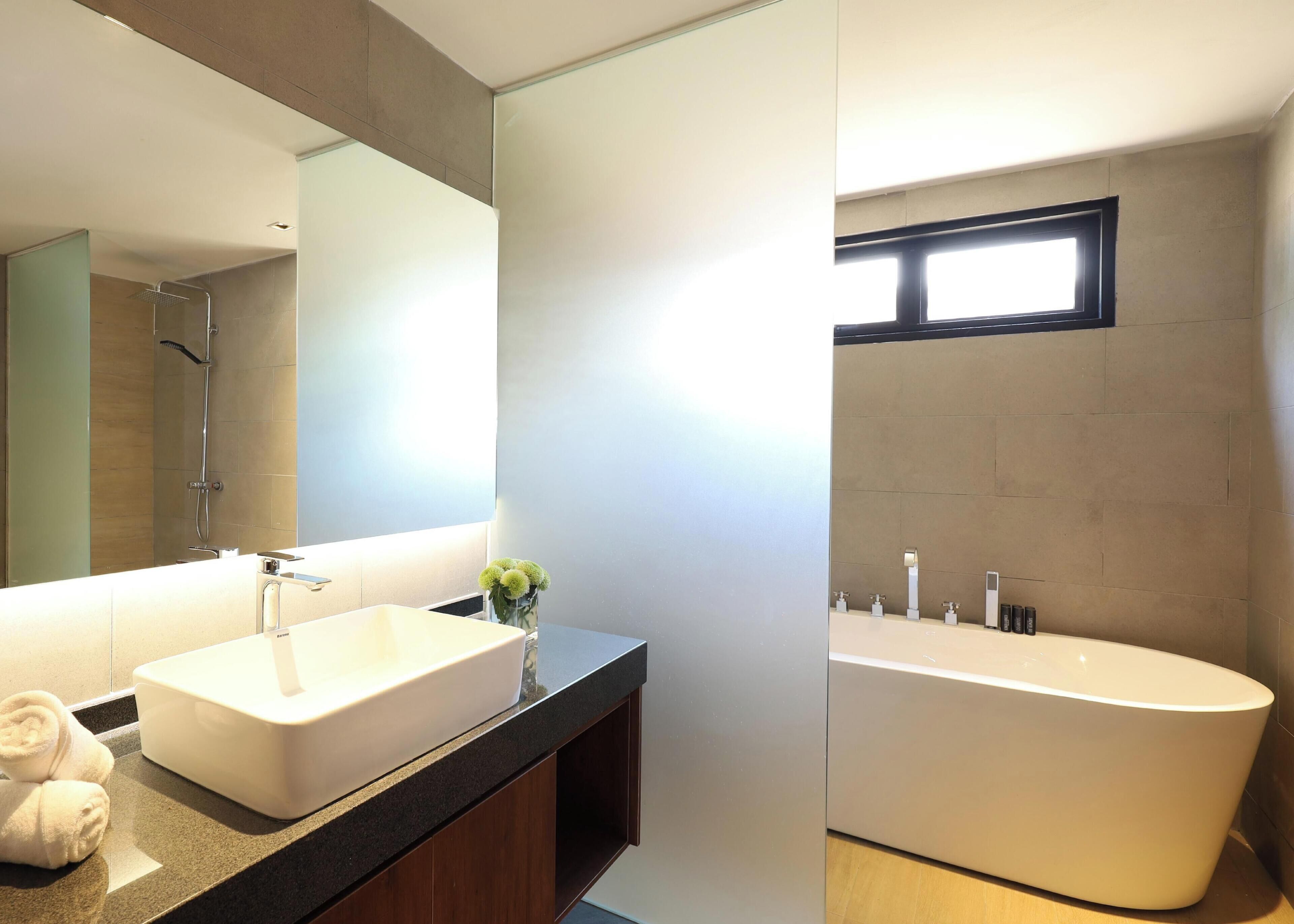 Un baño moderno con una bañera independiente grande, un lavamanos rectangular y un espejo sobre él.