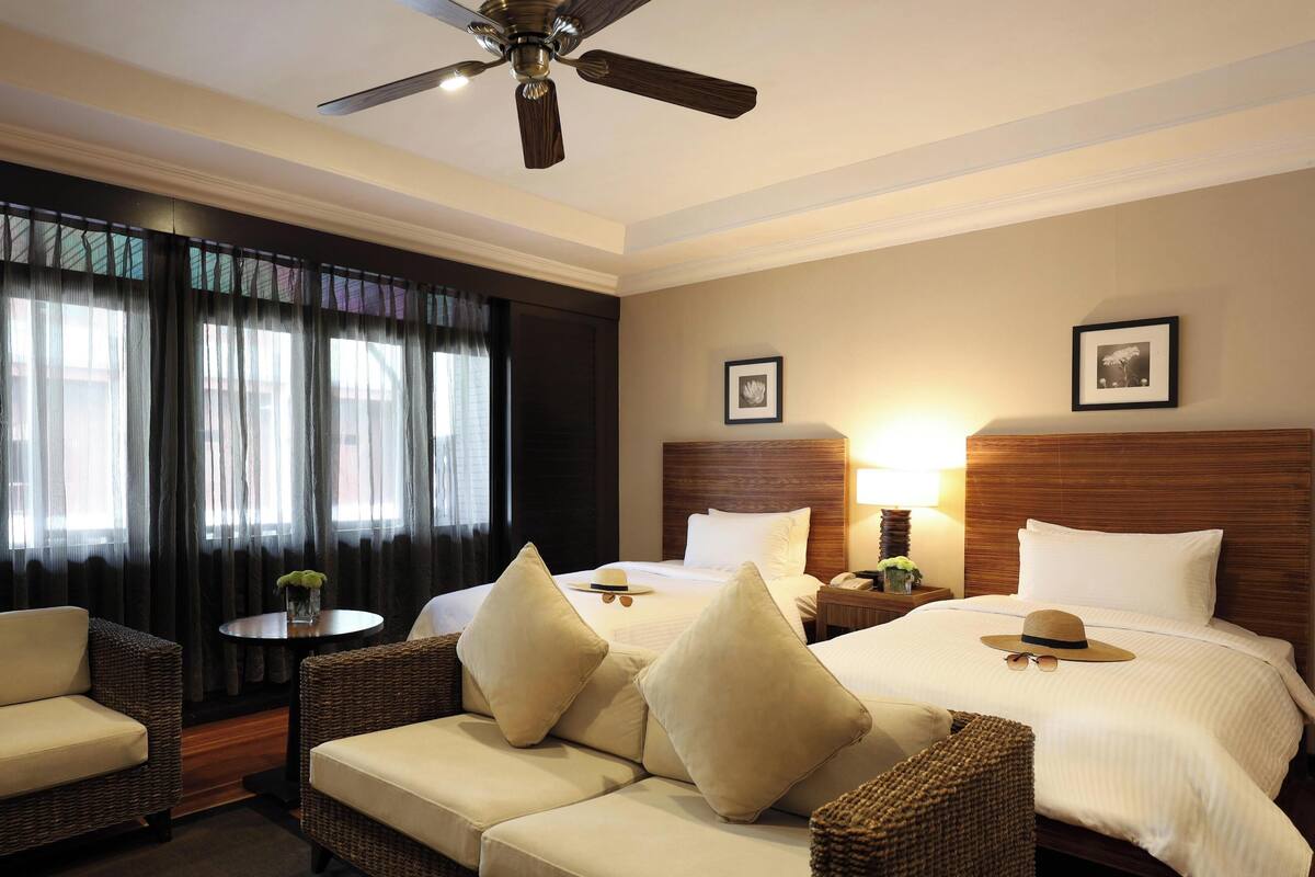 A hotel room with two beds, a sofa, a ceiling fan, and a window with curtains.