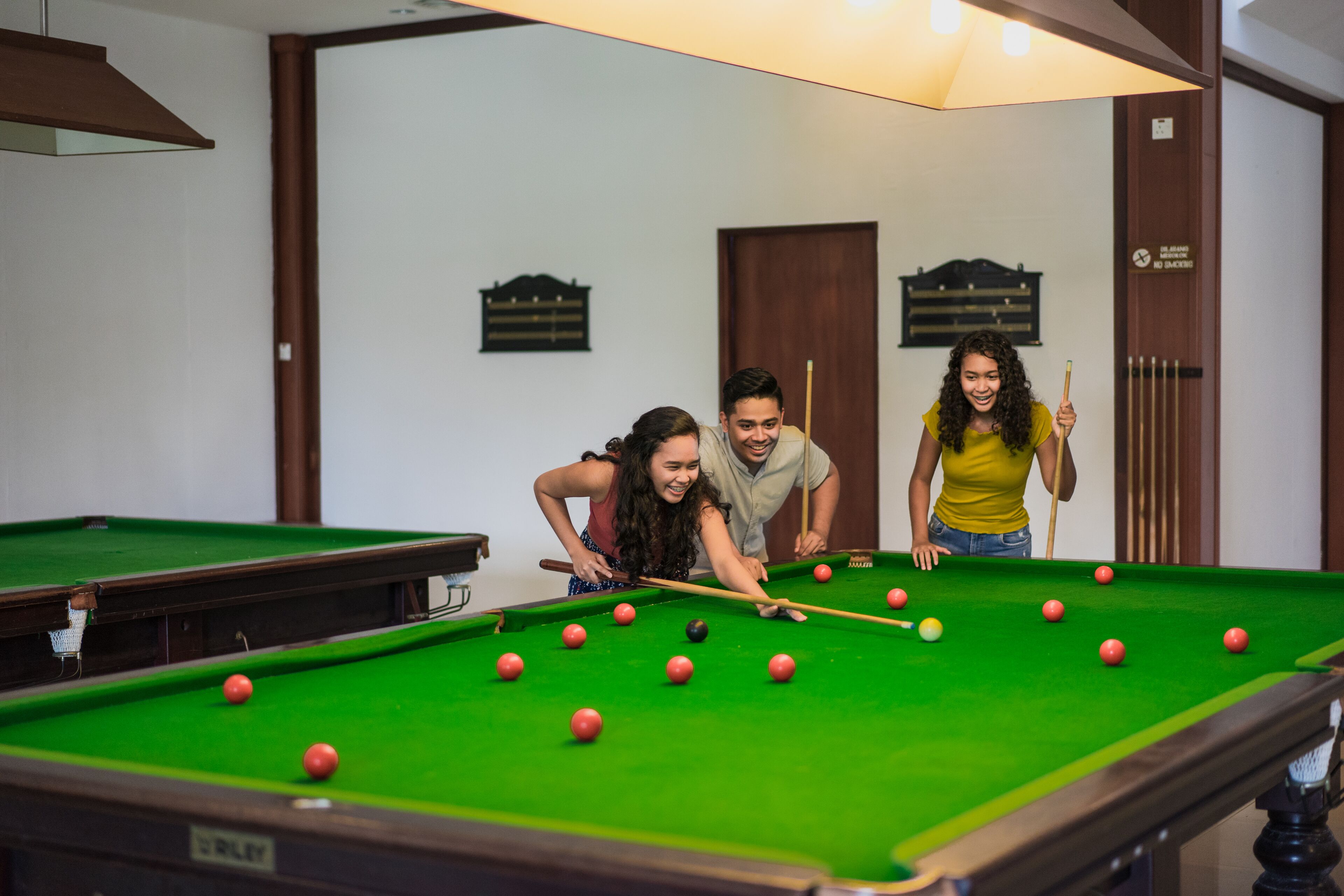 A pool table with balls, a person holding a cue stick, and a billiard rack in a room with wooden walls and a door.