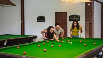 A pool table with balls, a person holding a cue stick, and a billiard rack in a room with wooden walls and a door.