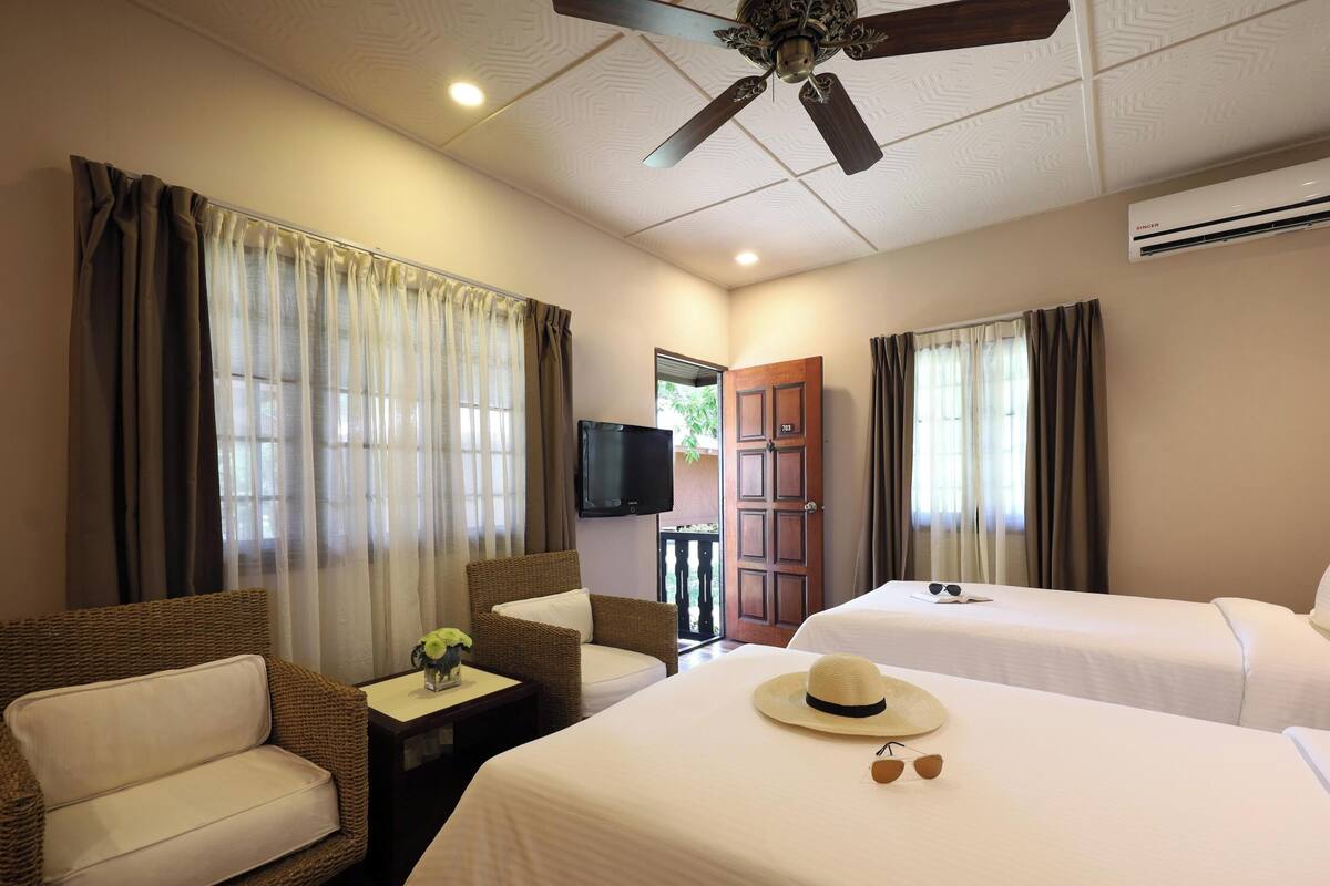 A hotel room with two beds, a television, a ceiling fan, and a door leading to an outdoor area.