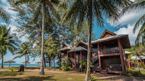 A resort with multiple wooden buildings, palm trees, and a beach view.
