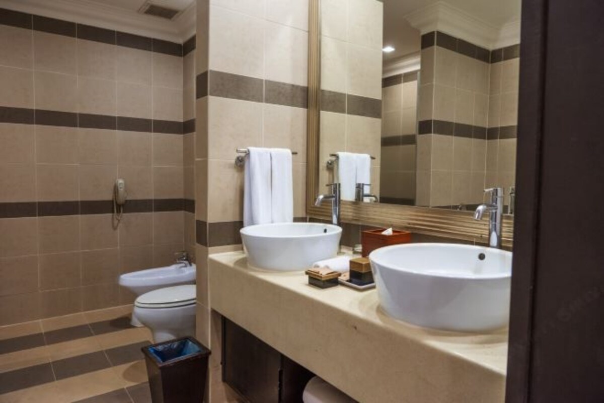 A modern bathroom with a toilet, two sinks, and a large mirror.