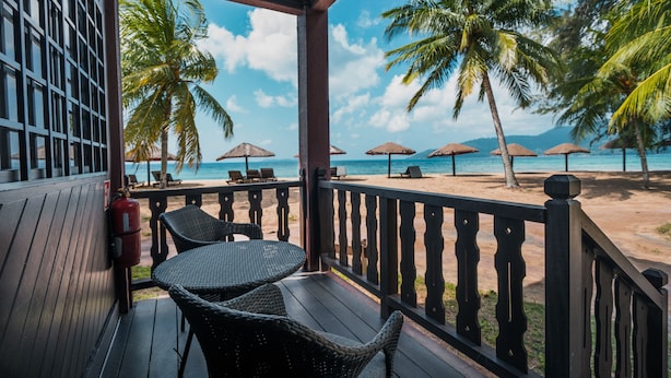 A beachside balcony with wicker chairs, a fire extinguisher, and umbrellas.